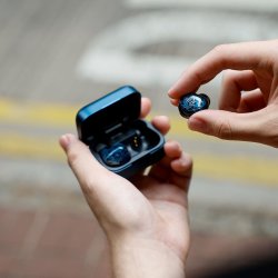 Et foto af en h�nd der tager en Noble Audio Osprey fra opladningsetuiet