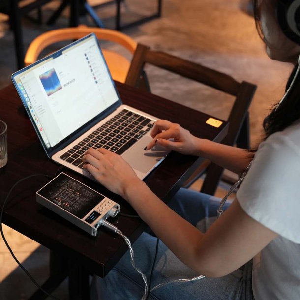 Questyle Sigma Pro i s�lv, ligger p� et bord ved siden af en computer